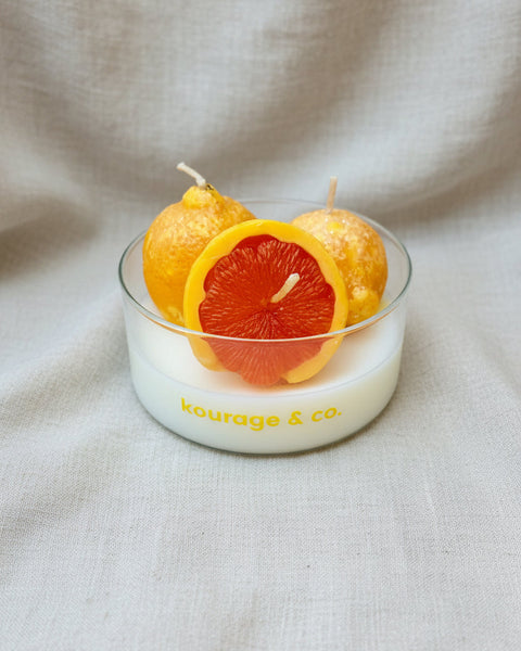 Candle with orange slices and lemons in a glass bowl on a textured brown background