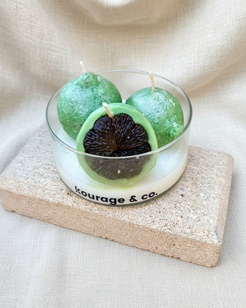 Three green candles in a glass holder on a textured surface with 'Courage & co.' branding.