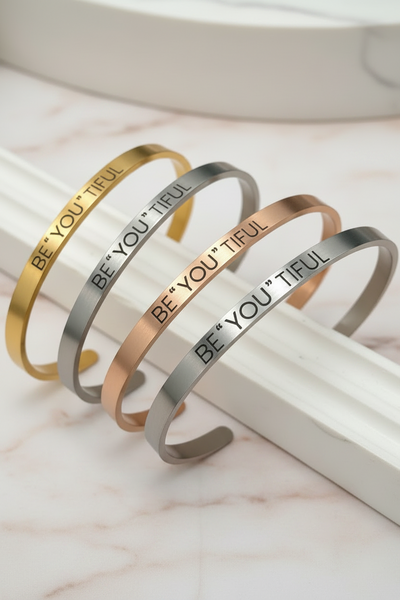 Three bracelets with 'BE YOU TIFUL' text on a marble surface