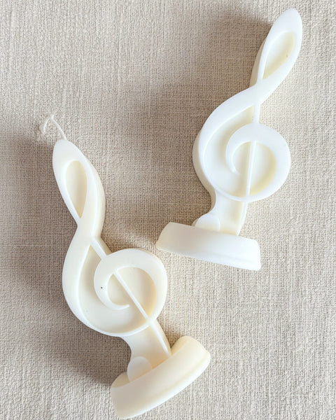 Two white plastic novelty candles shaped like musical treble clefs, displayed on a textured brown burlap fabric background.