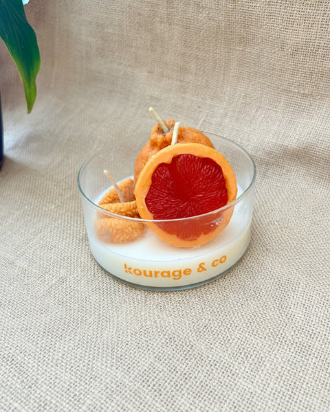 Candle with grapefruit design in a glass holder on a textured surface