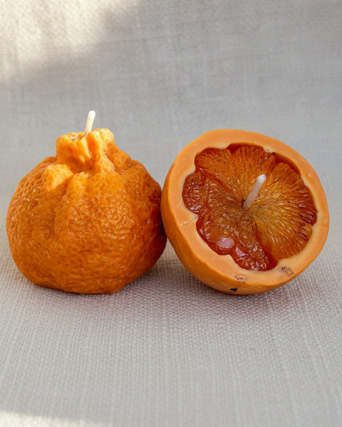Two orange peel candles on a textured fabric background