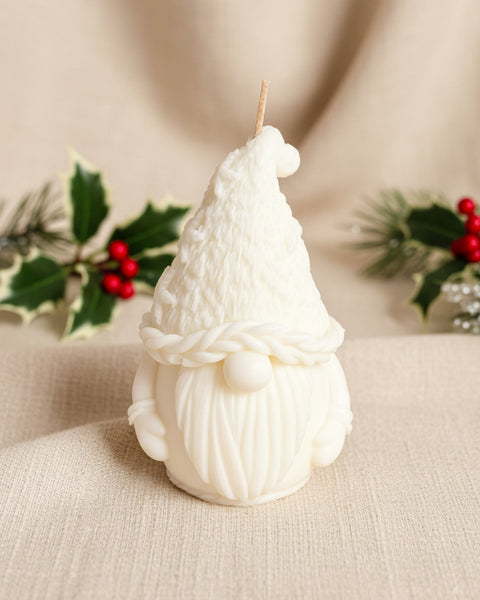 A white gnome figurine candle with a textured knit hat, braided neck detail, and long beard, standing on a brown burlap fabric background.