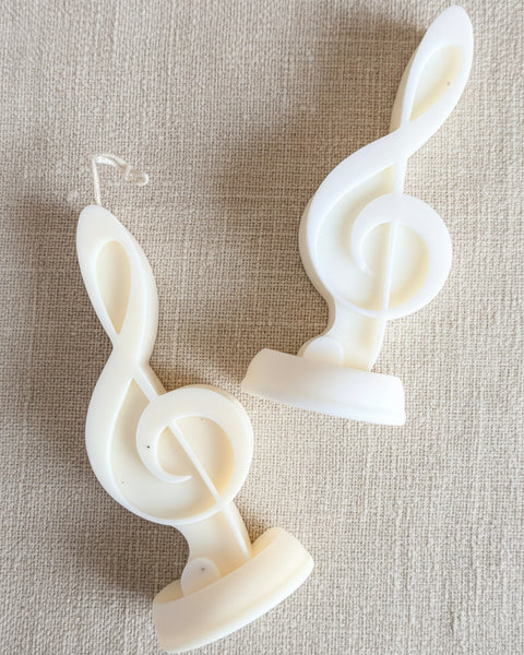 Two white plastic novelty candles shaped like musical treble clefs, displayed on a textured brown burlap background.