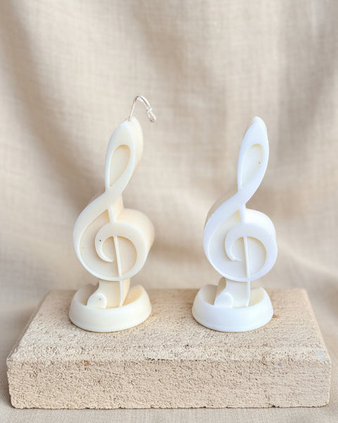 Two white musical treble clef candles displayed on a rectangular stone block against a burlap backdrop.