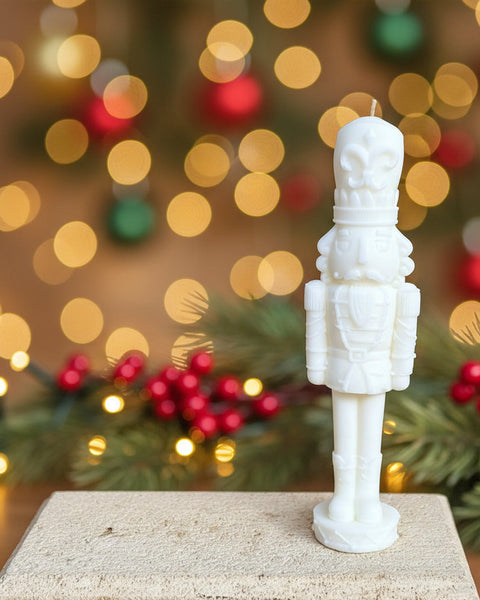 A white nutcracker candle standing upright on a light stone block against a textured burlap backdrop.
