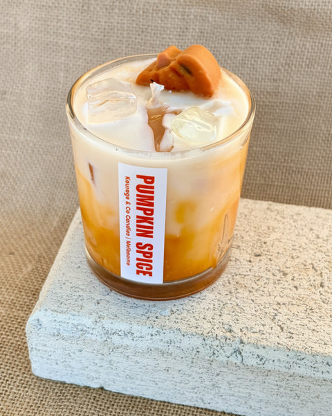 An iced coffee drink in a clear glass cup with a white label reading 'Pumpkin Spice' and 'Energy Co. Coffee Roasters,' topped with a pumpkin pie slice, set on a stone slab against a burlap backdrop.