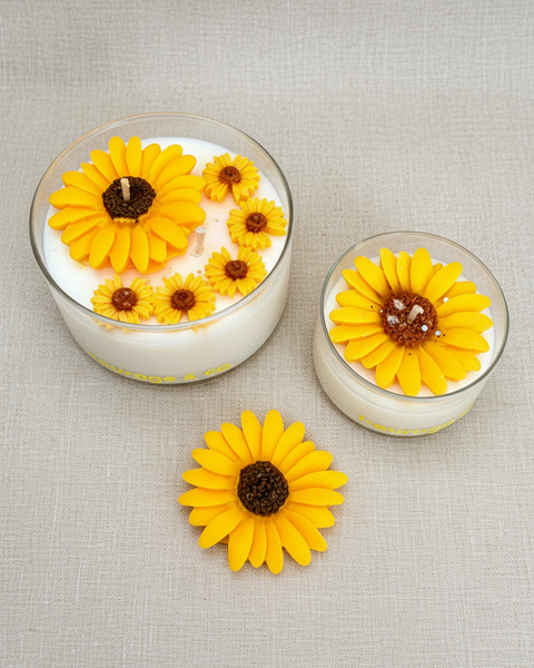 Two small glass containers with yellow flower-shaped candles on a textured brown fabric background.
