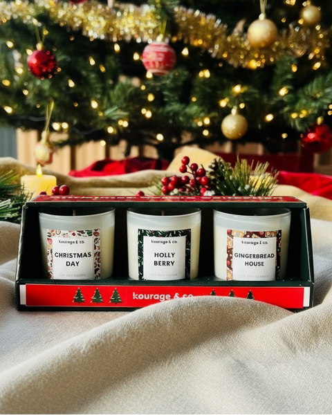 Three small candles in a decorative box with Christmas-themed labels on a soft surface.