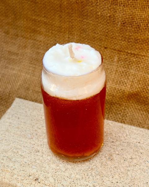 Candle in a glass jar with a white wick on a textured surface and brown background