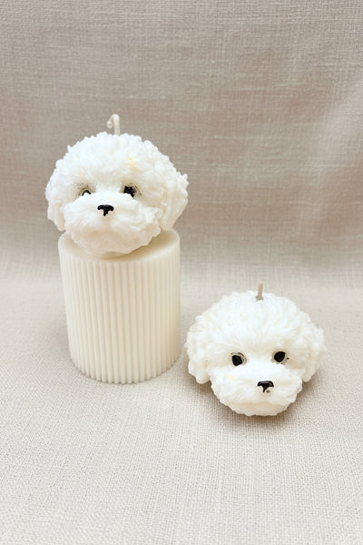 Two white dog-shaped candles on a brown fabric background