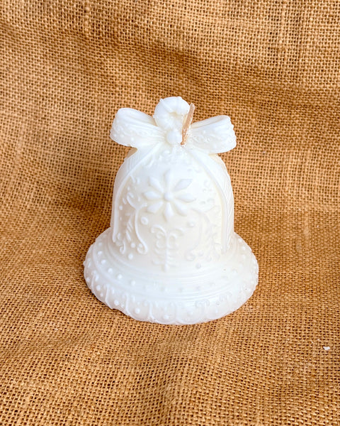 A white decorative glass bell ornament with embossed floral patterns and a bow on top, displayed on a textured burlap background.