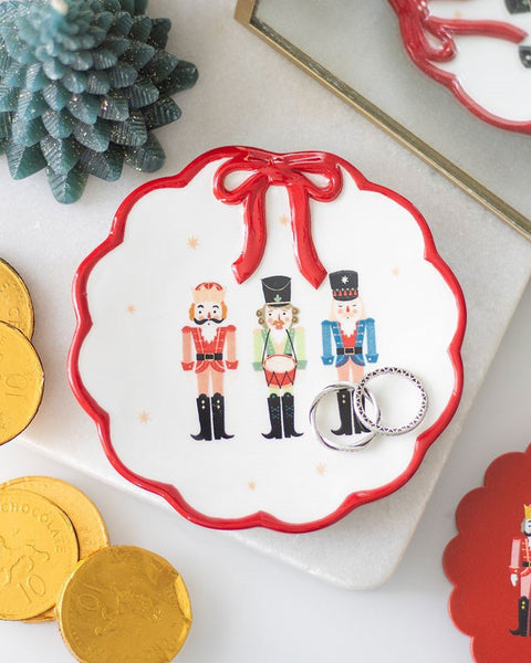 Decorative dish with nutcracker design surrounded by gold coins and a small pine tree decoration.