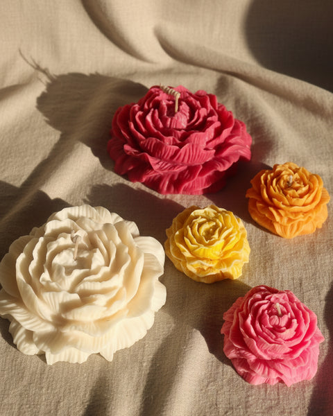 Five flower-shaped soaps in pink, white, yellow, and orange on a textured fabric background.